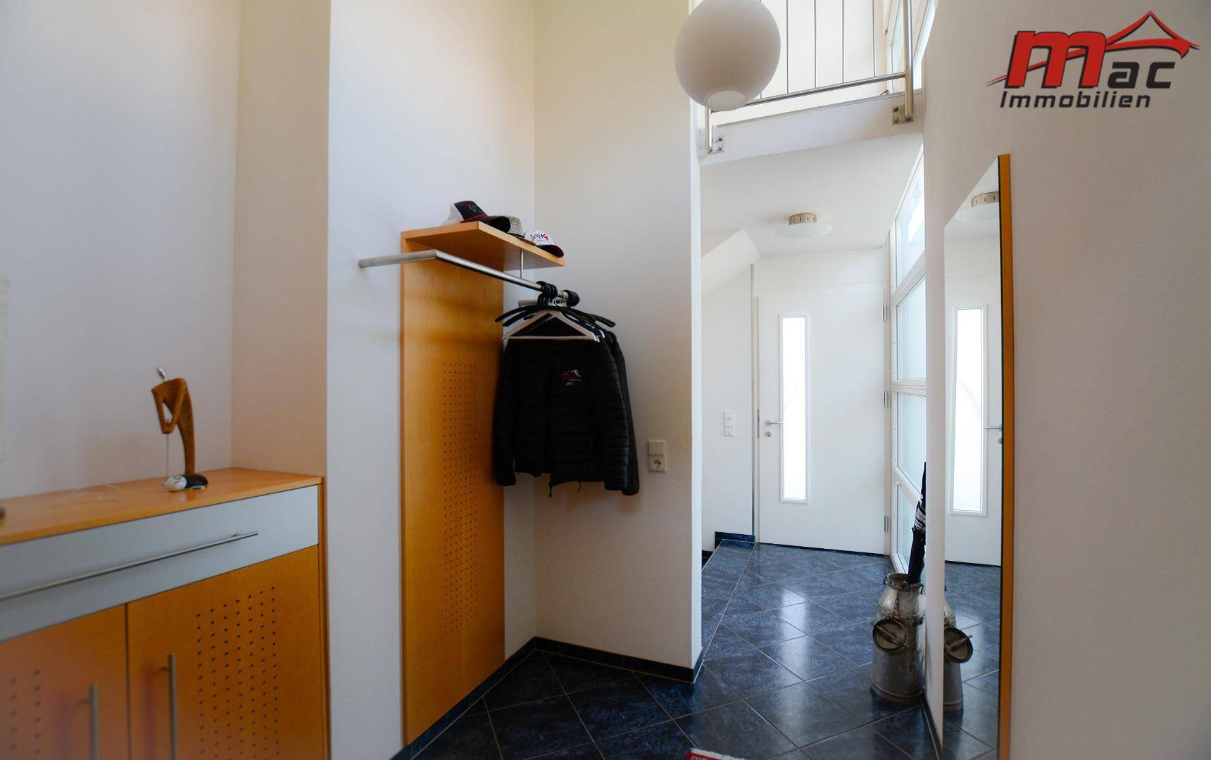 Heller Eingangsbereich mit dunklen Fliesen, Garderobe und einem Spiegel, der den Raum erweitert.