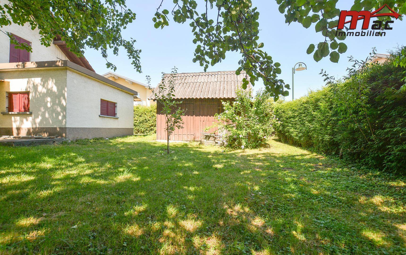Großer, gepflegter Garten mit Rasenfläche, Hecke und einem kleinen Holzschuppen.