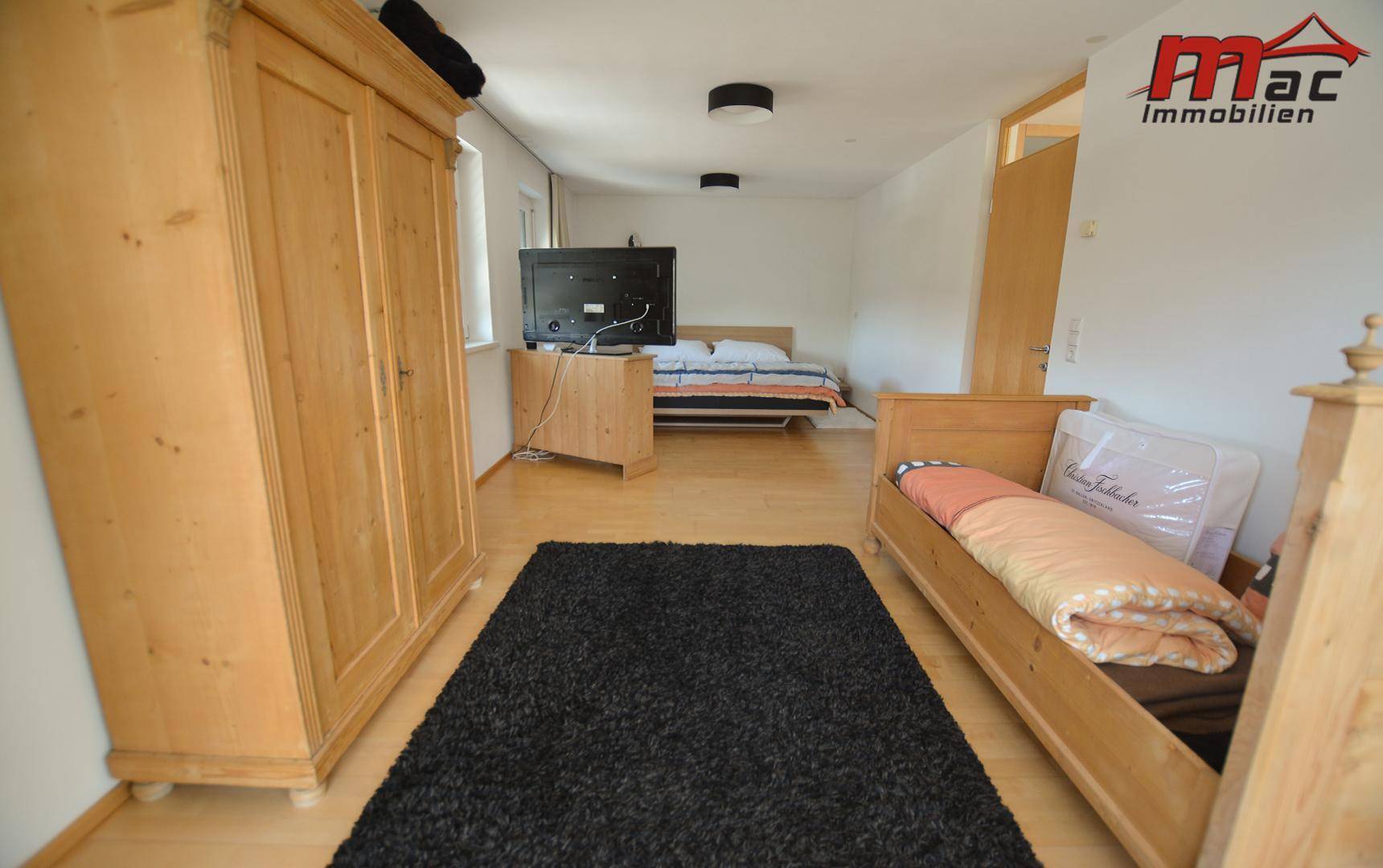 Helles Schlafzimmer mit Holzboden, Holzmöbeln und einem weiteren Bett im Hintergrund.