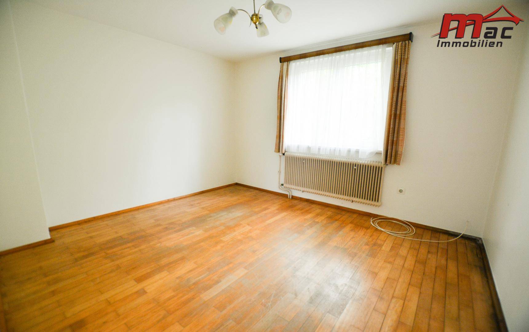 Leeres Zimmer mit hellem Parkettboden und großem Fenster, bereit zur individuellen Gestaltung.
