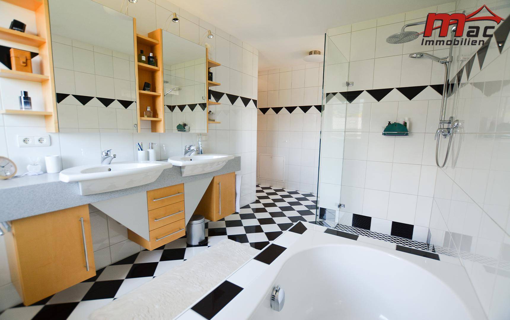 Geräumiges Badezimmer mit Doppelwaschbecken, großer Dusche und schwarz-weißen Fliesen.