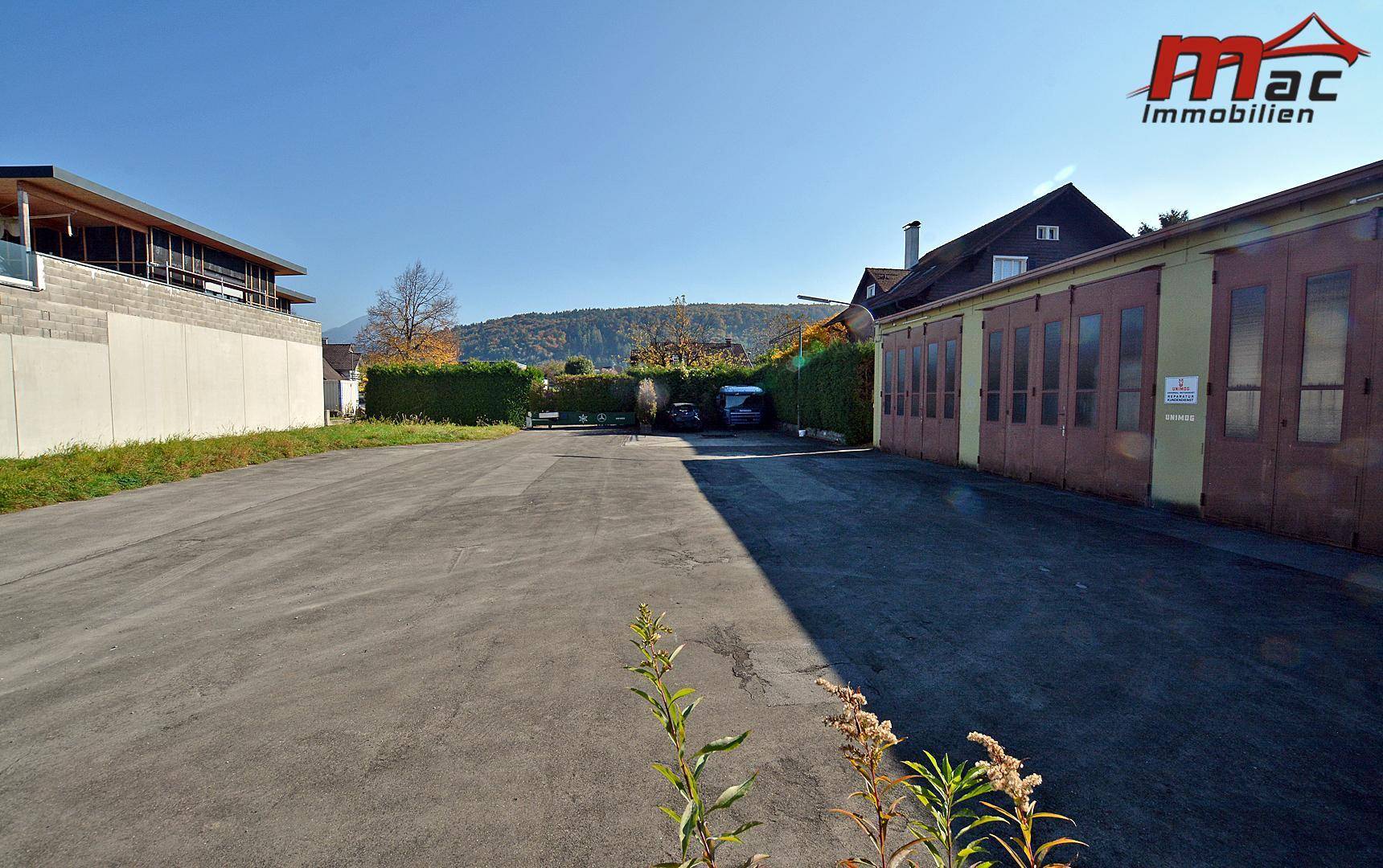 Ausgedehnte befestigte Fläche zwischen Gebäuden mit Blick auf die bewaldeten Hügel in der Ferne.