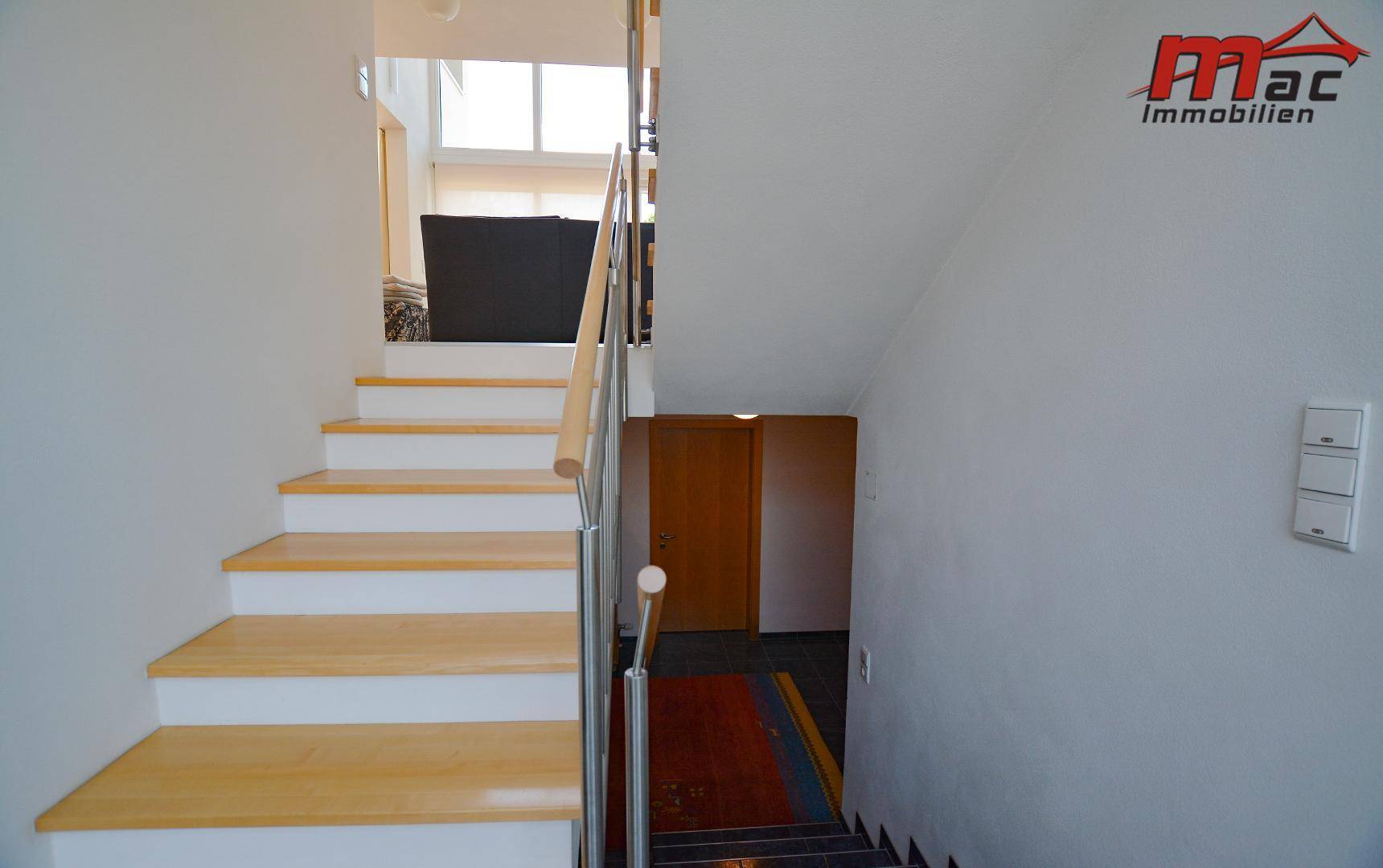 Heller Treppenaufgang mit Holzstufen und Edelstahlgeländer, der verschiedene Ebenen verbindet.