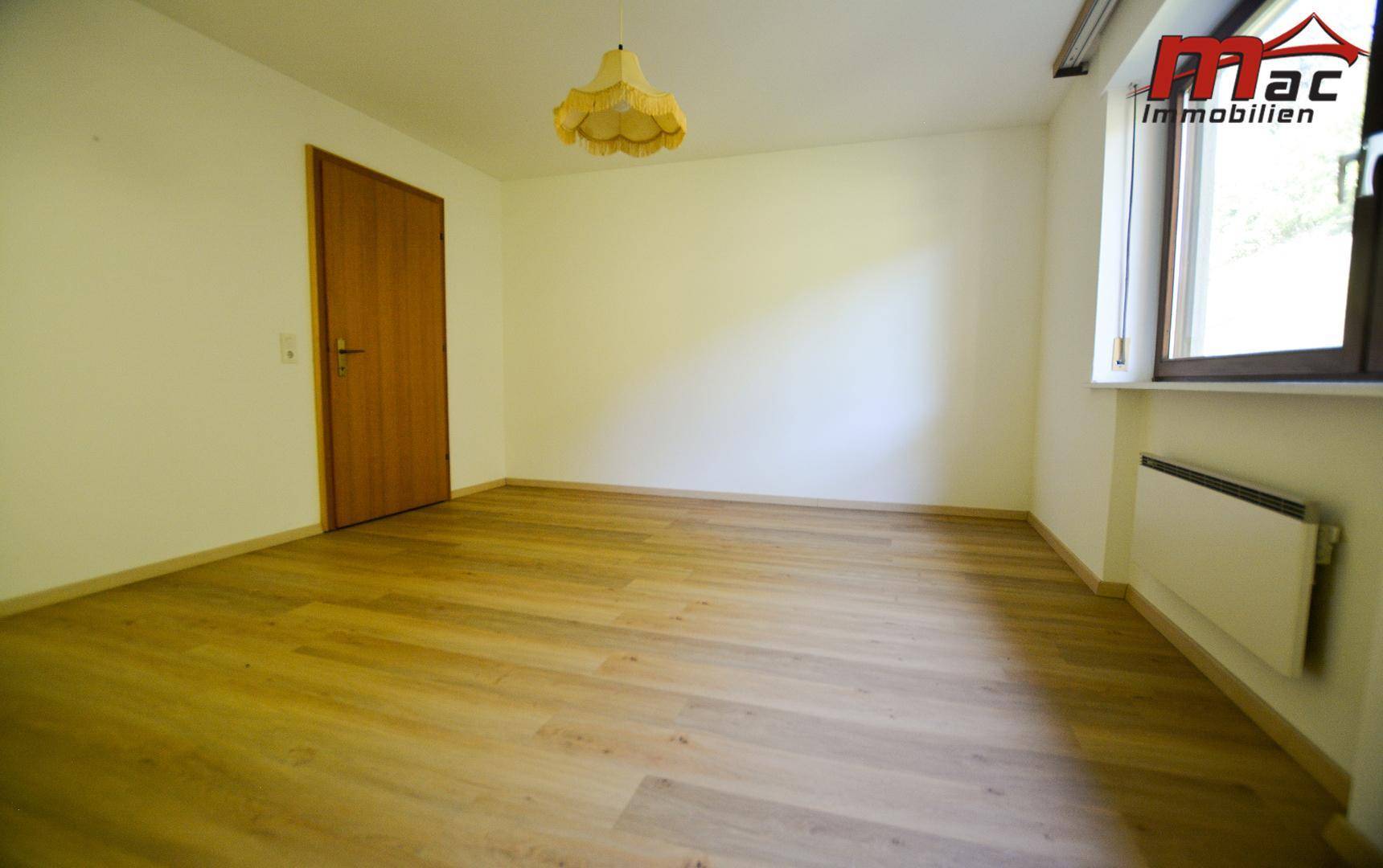 Leerer Raum mit hellem Laminatboden und Fenster, ideal für verschiedene Nutzungsmöglichkeiten.