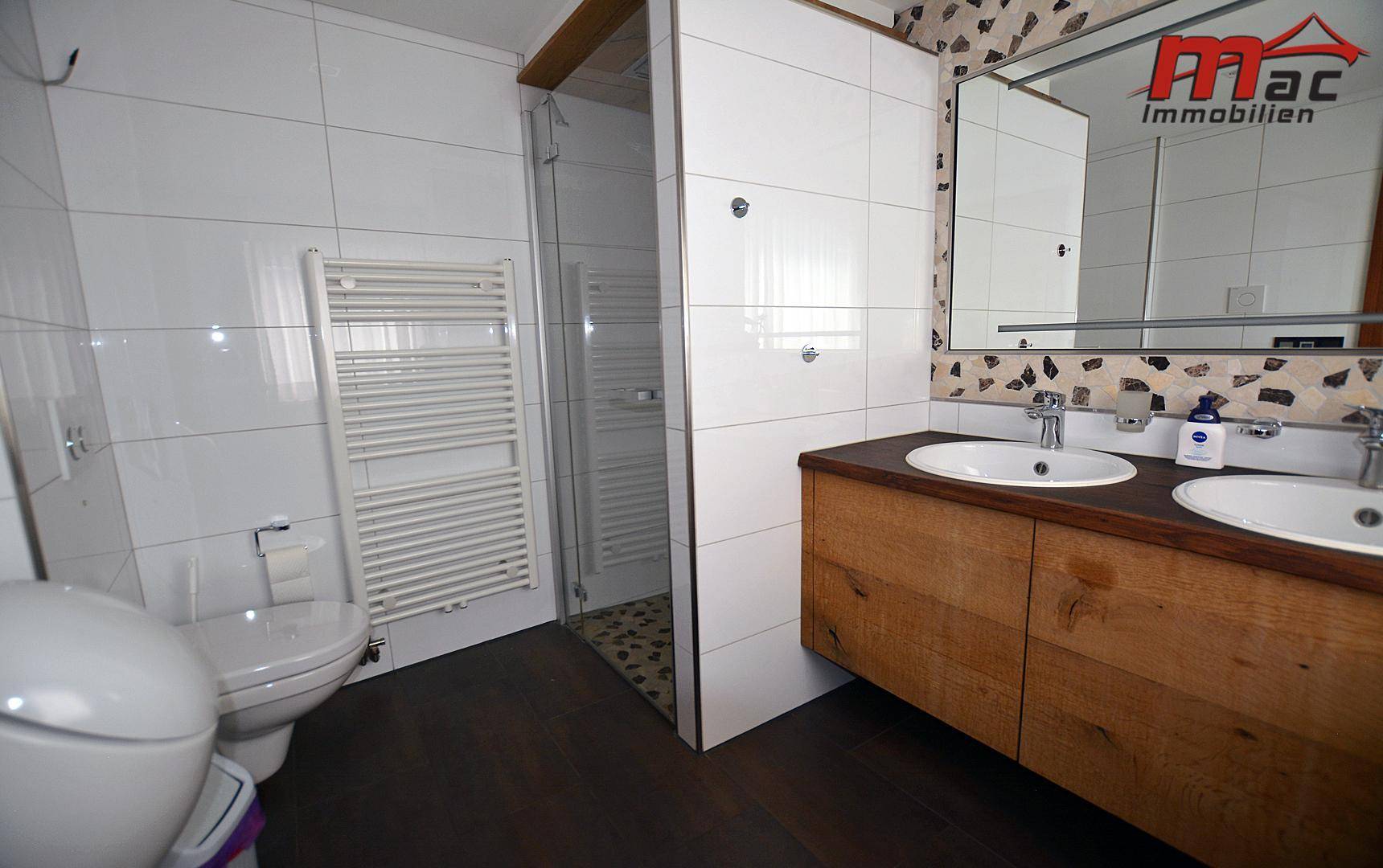Modernes Badezimmer mit Doppelwaschbecken, Holzelementen und begehbarer Dusche.