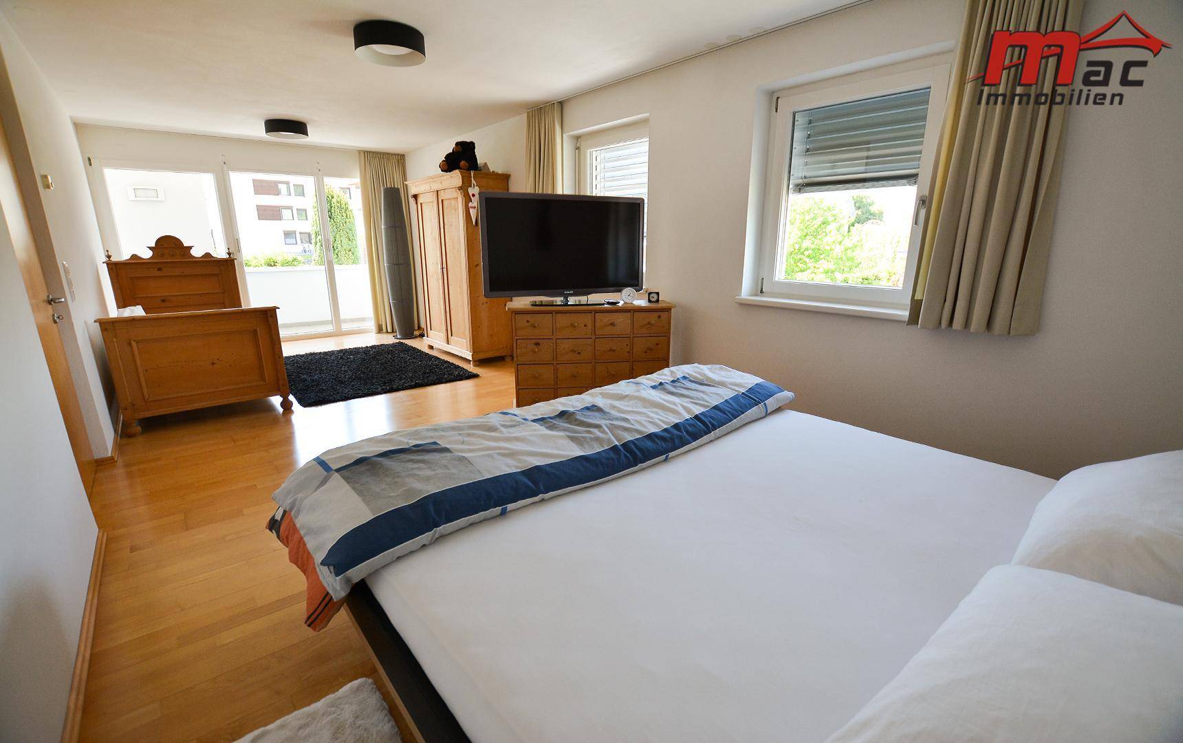 Geräumiges Schlafzimmer mit zwei Betten, Holzboden und Zugang zu einem Balkon.