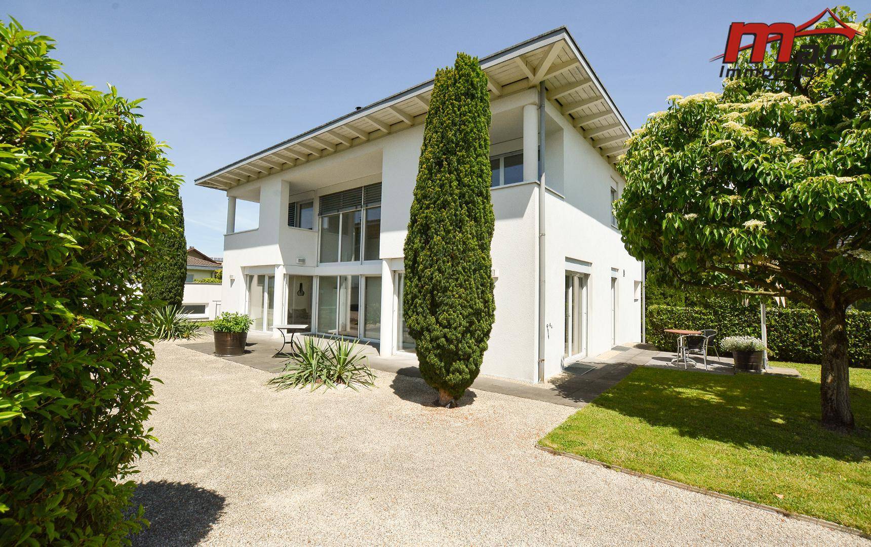Moderne Villa mit großen Fensterfronten und gepflegtem Gartenbereich unter blauem Himmel.