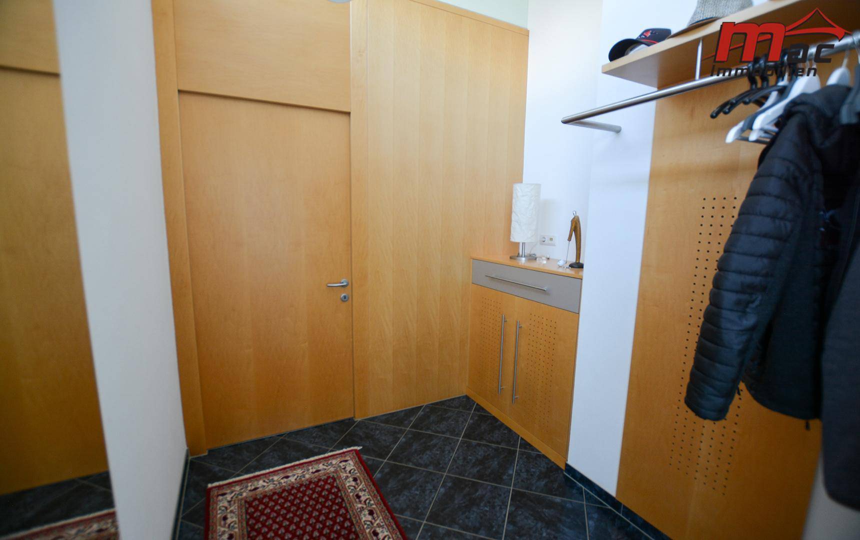 Eingangsbereich mit dunklen Fliesen, Holzverkleidung und einer praktischen Garderobenlösung.