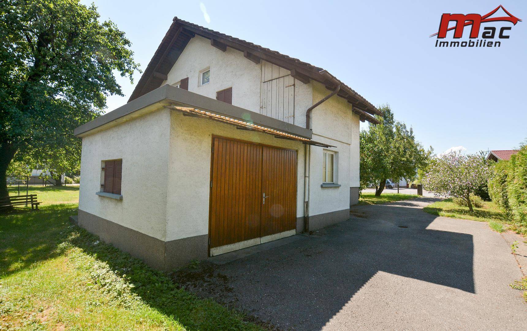Seitenansicht des Hauses mit integrierter Garage und asphaltierter Zufahrt.