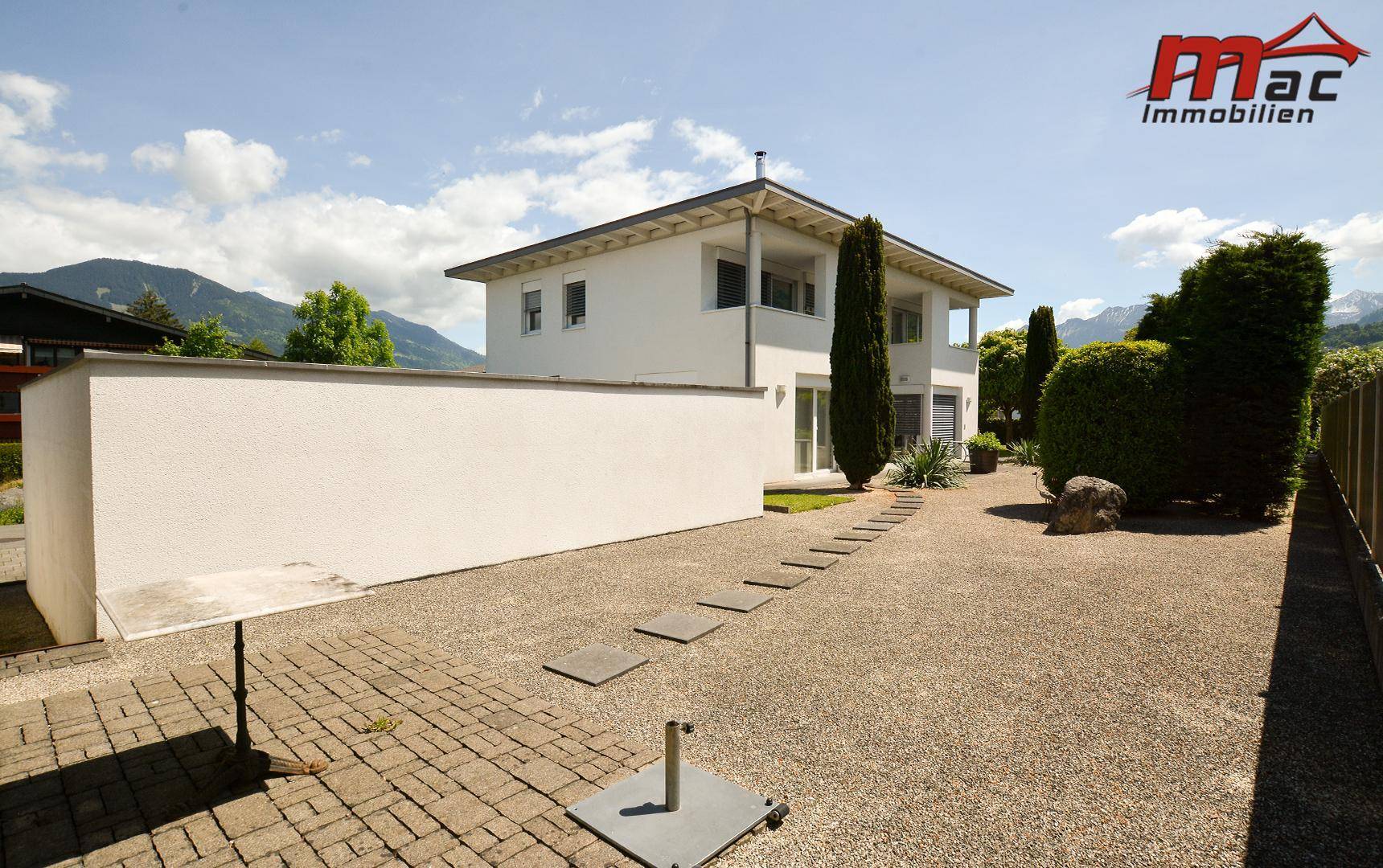 Moderne Hausfassade mit weißem Putz und weitläufigem Kiesgarten im Vordergrund.