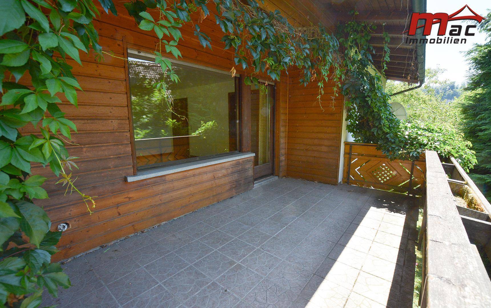 Überdachte Terrasse mit Holzverkleidung und Fliesenboden, bietet direkten Zugang zum Innenbereich.