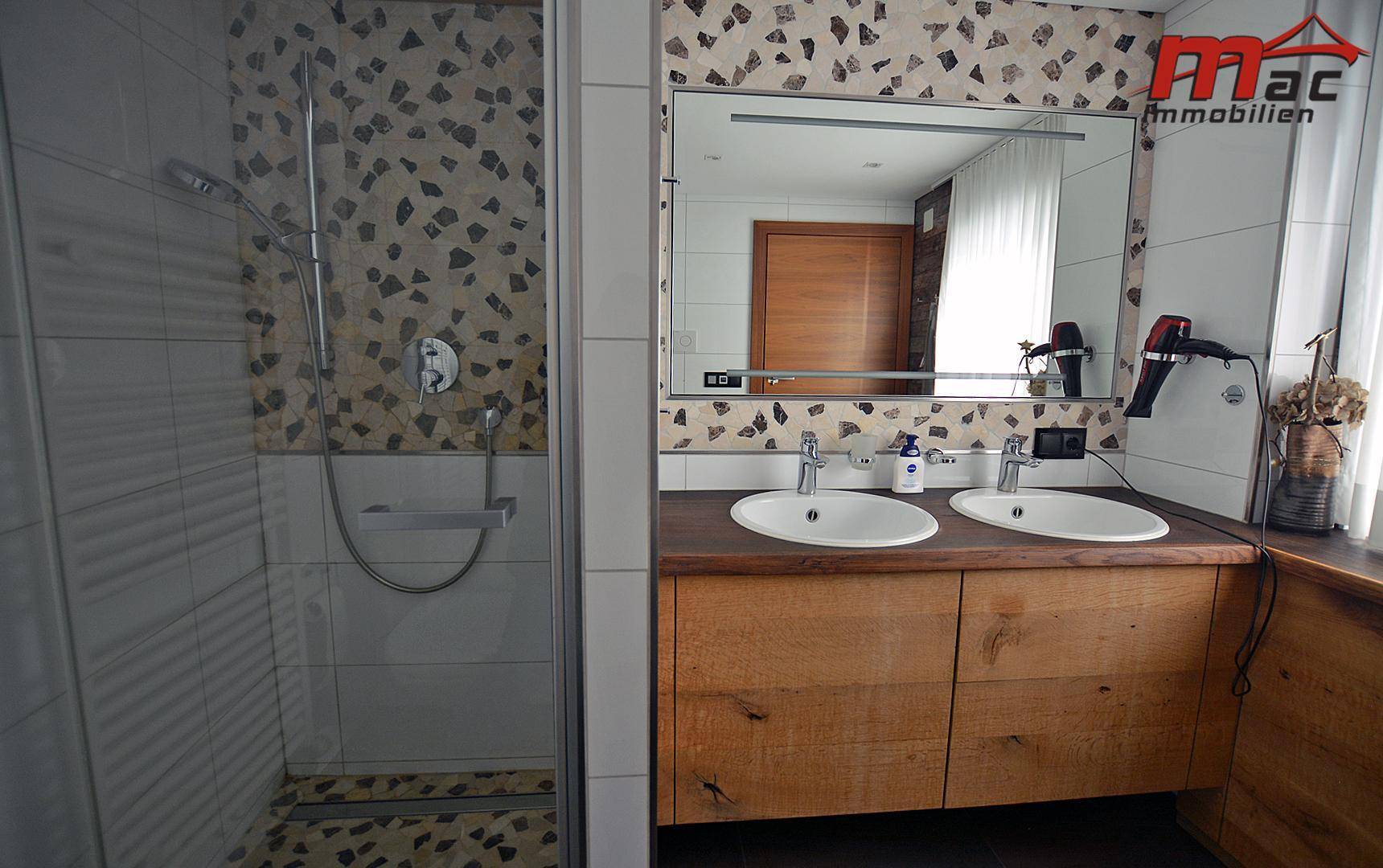 Badezimmer mit begehbarer Dusche, Doppelwaschbecken und modernem Fliesenmuster an der Wand.