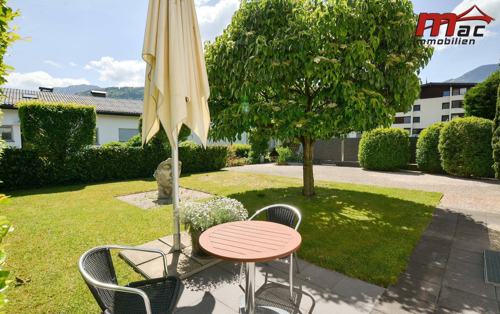 Gemütlicher Sitzbereich im Garten mit Sonnenschirm, Tisch und Stühlen auf dem Rasen.
