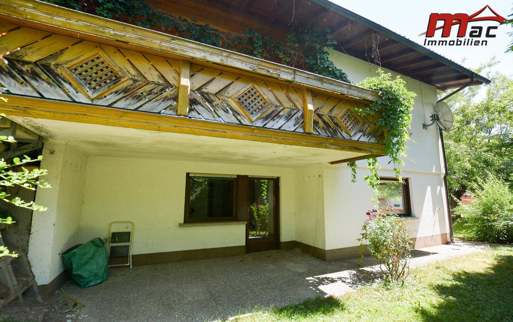 Überdachte Terrasse im Erdgeschoss unter einem traditionellen Holzbalkon mit dekorativem Geländer.