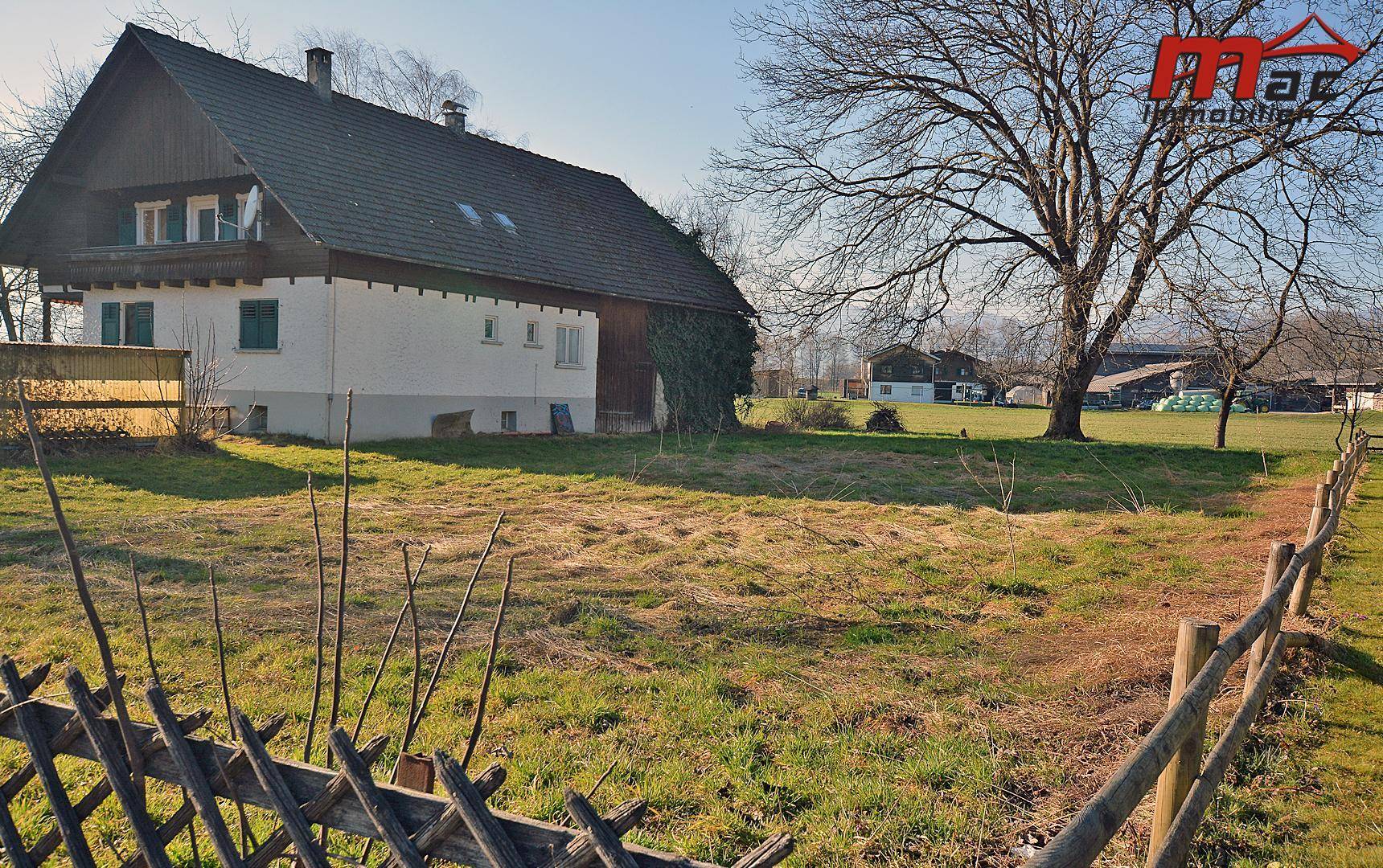 Haus mit großem Garten und Holzzaun, umgeben von Natur und ländlicher Idylle.