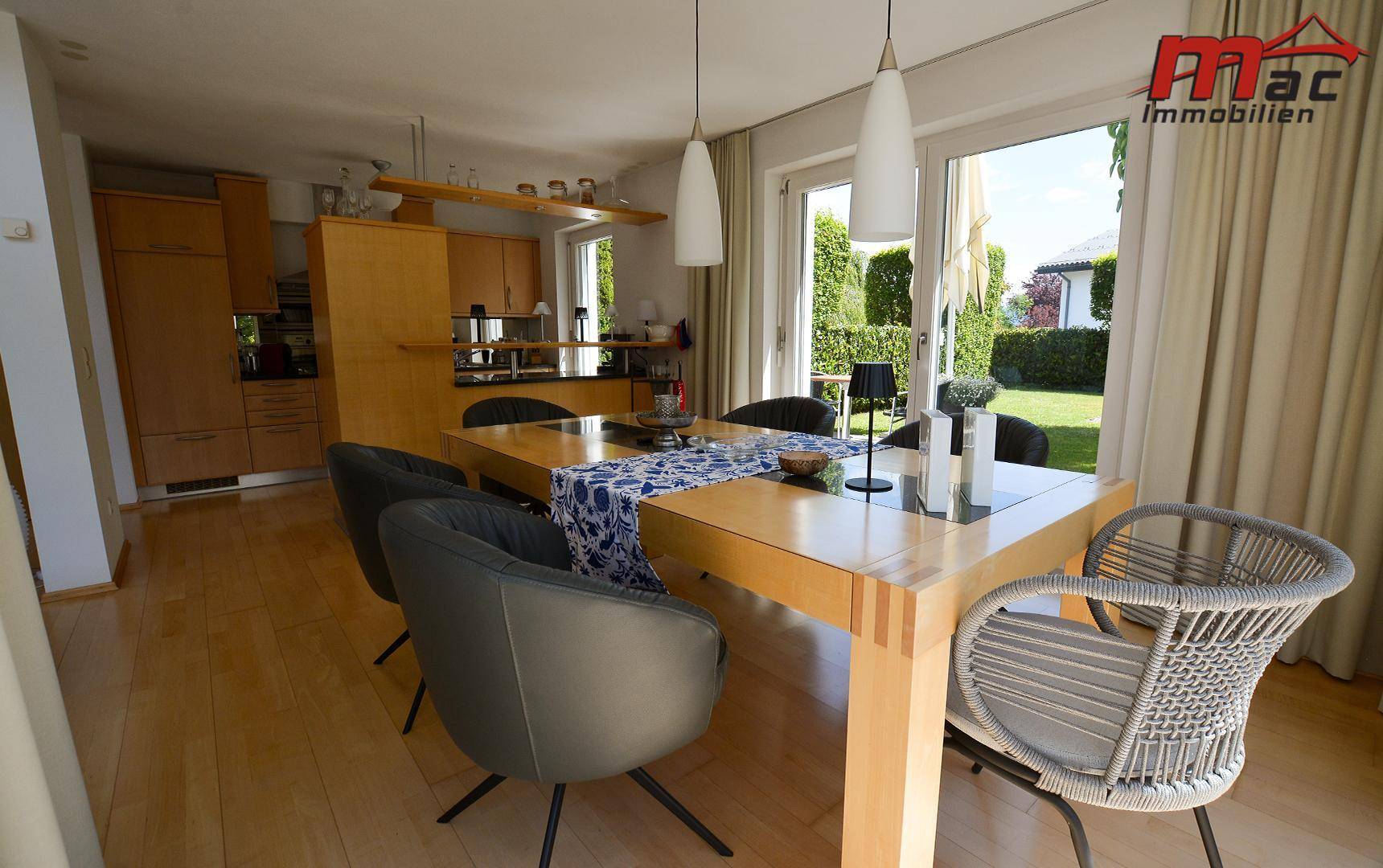 Essbereich mit Holztisch, modernen Stühlen und Blick auf die offene Küche und den Garten.