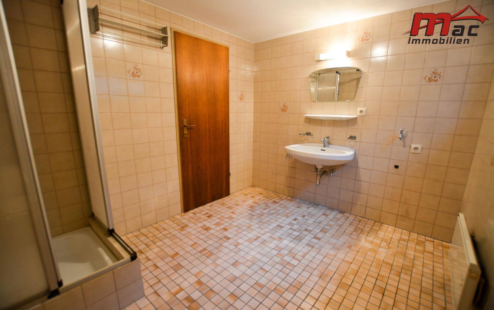 Badezimmer mit beigefarbenen Fliesen, Waschbecken, Spiegelschrank und einer Duschkabine.