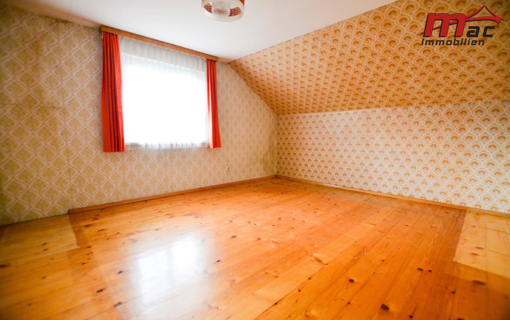 Schlafzimmer im Dachgeschoss mit schräger Decke, Holzboden und gemusterter Tapete.