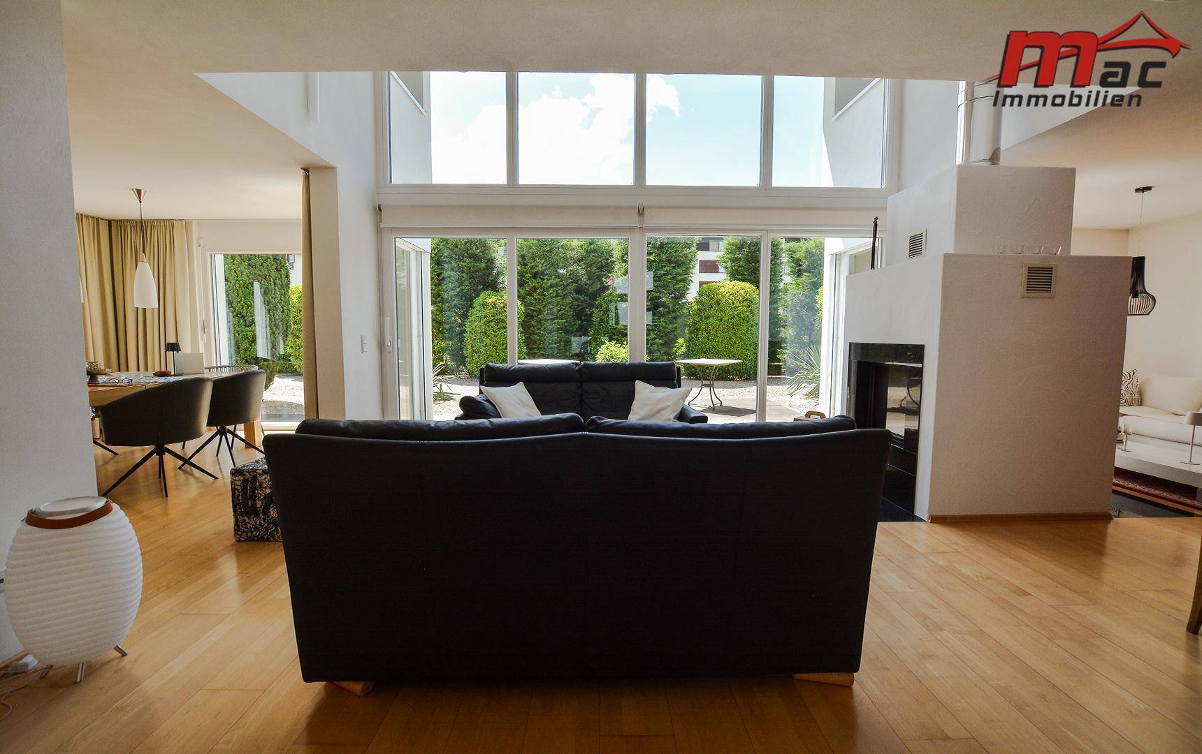 Großzügiges Wohnzimmer mit Holzboden, Kamin und bodentiefen Fenstern zum Garten.