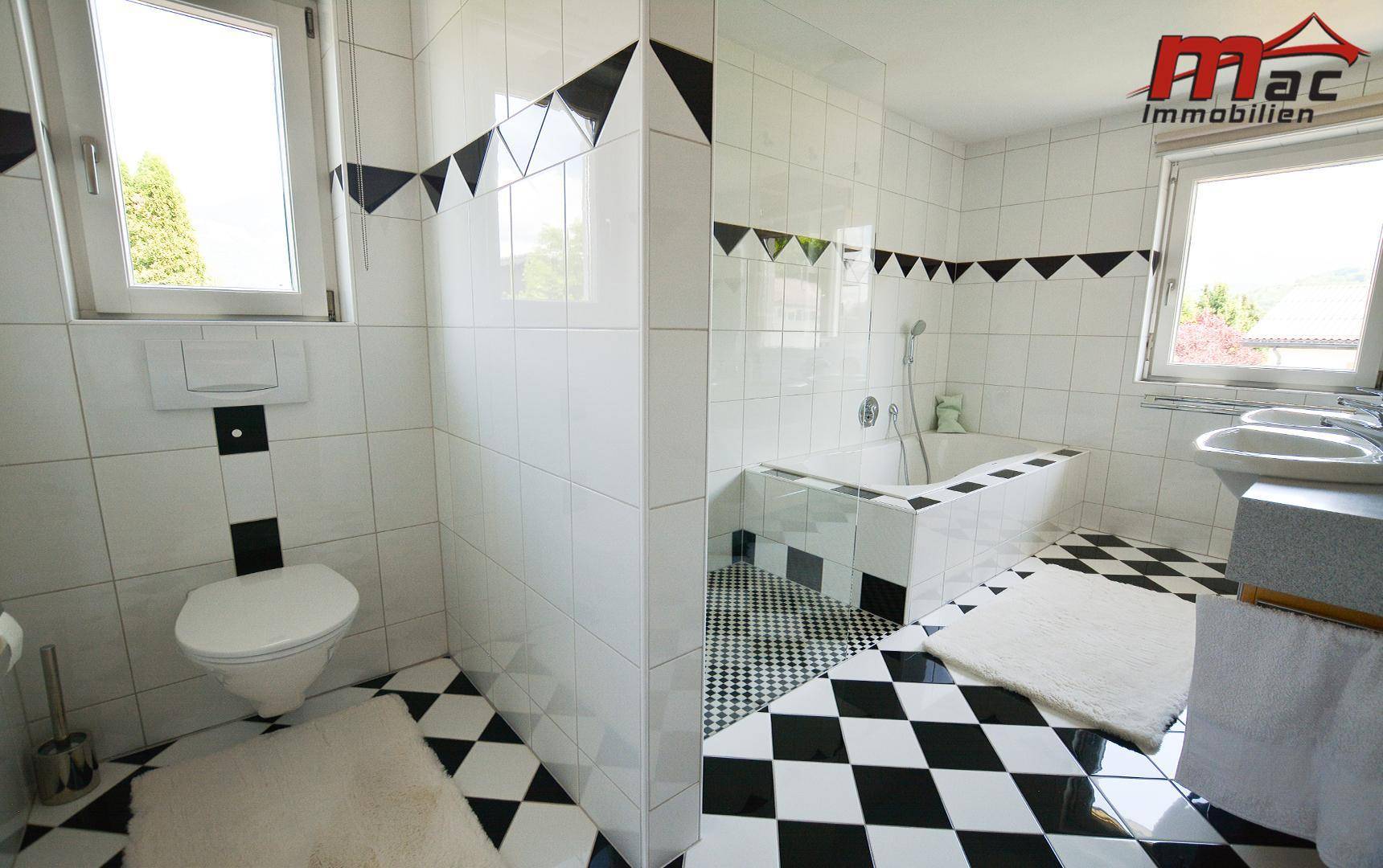 Badezimmer mit markanten schwarz-weißen Fliesen, Badewanne und Fenster.