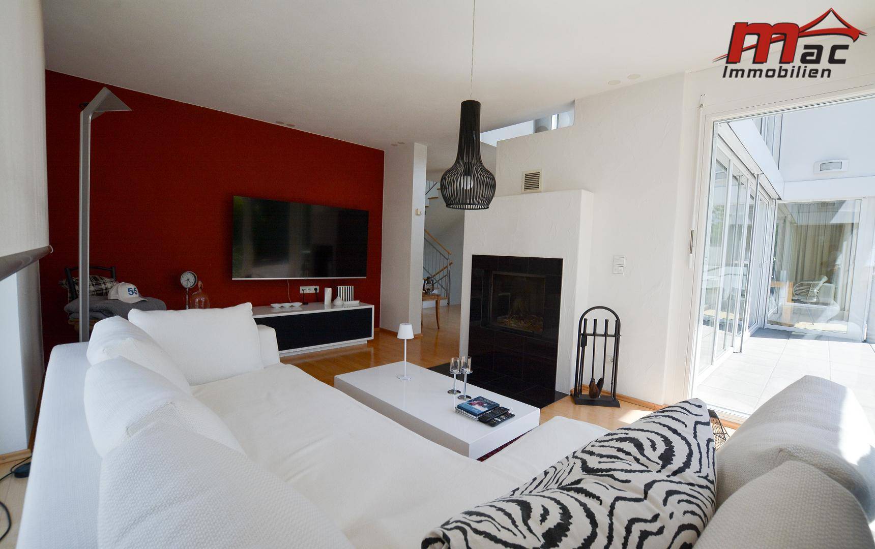 Modernes Wohnzimmer mit roter Akzentwand, weißem Sofa und Kamin, offen und lichtdurchflutet.