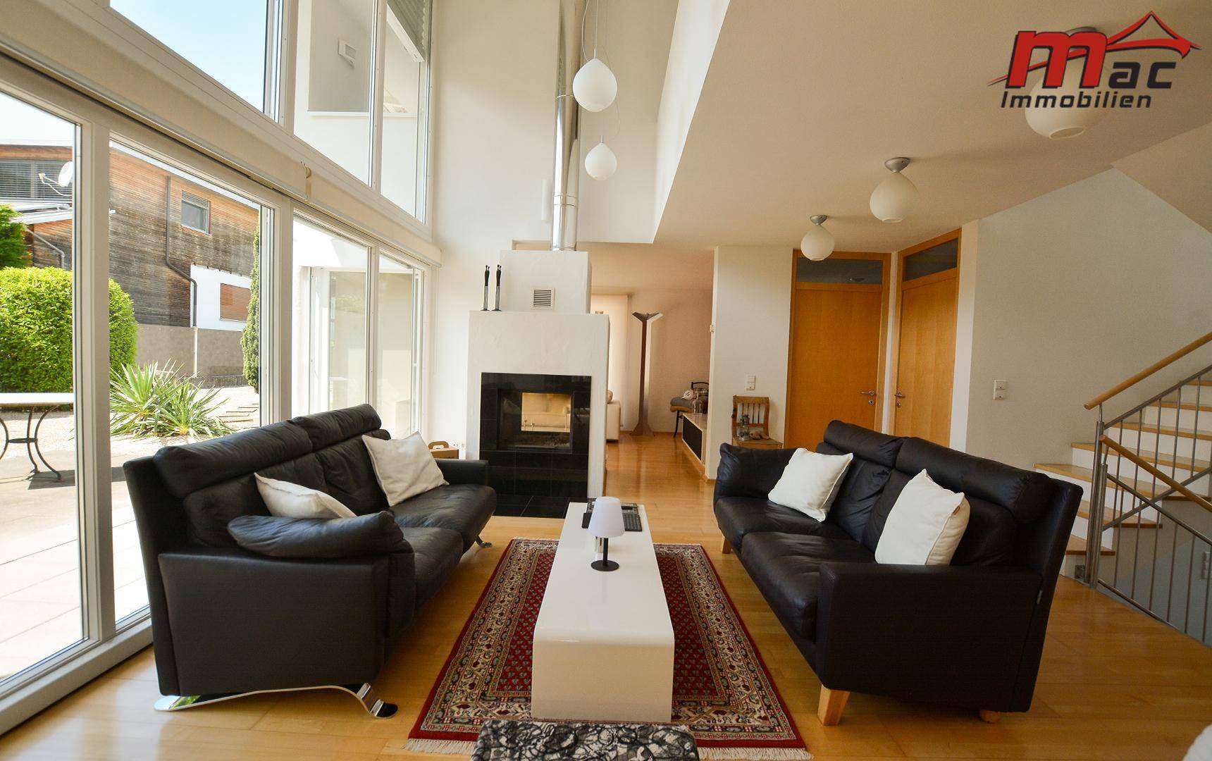Helles Wohnzimmer mit Kamin, Holzboden und großen Fensterfronten zum Garten.