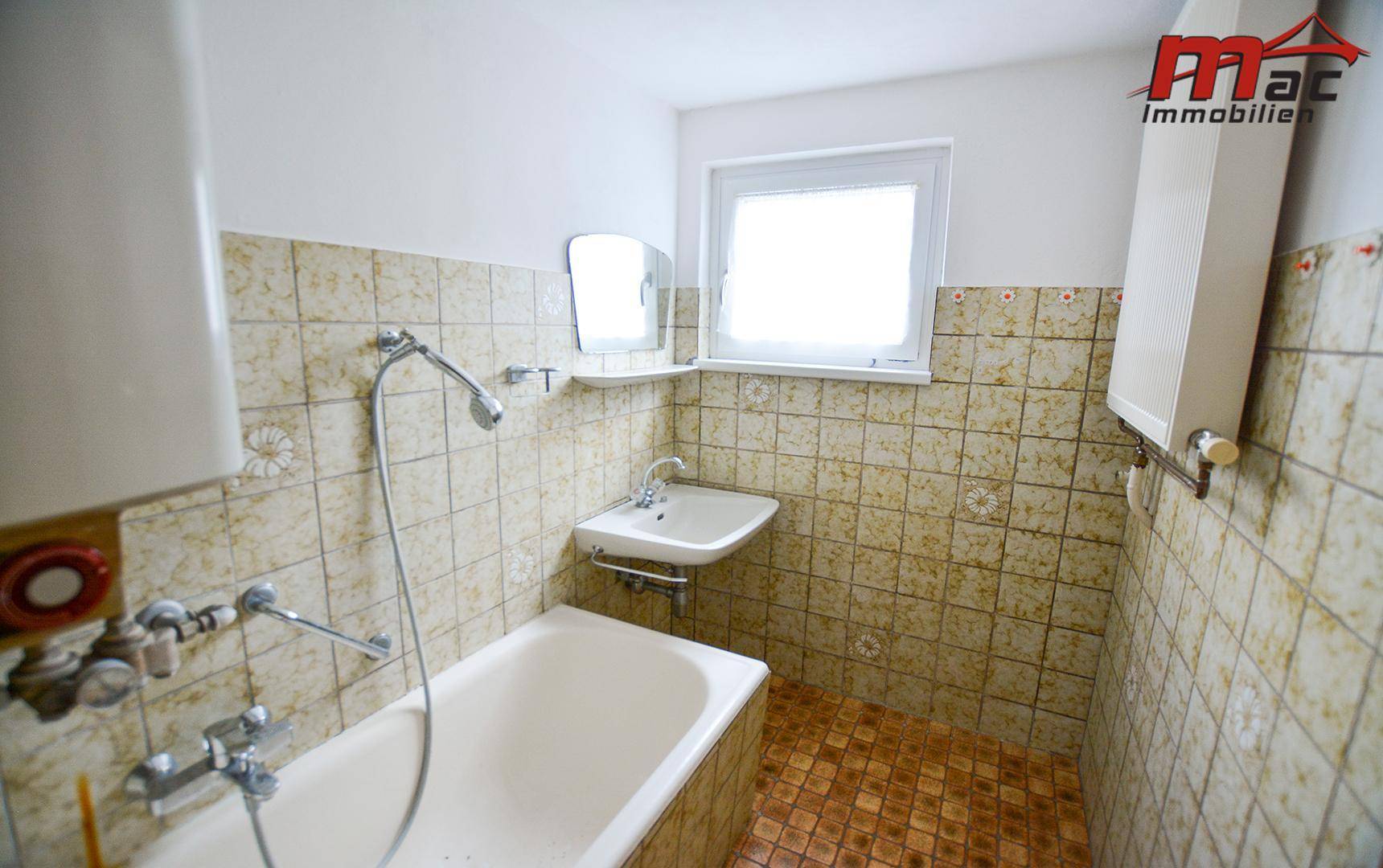 Badezimmer mit Badewanne, Waschbecken und Fenster, ausgestattet mit Fliesen im 80er-Jahre-Stil.