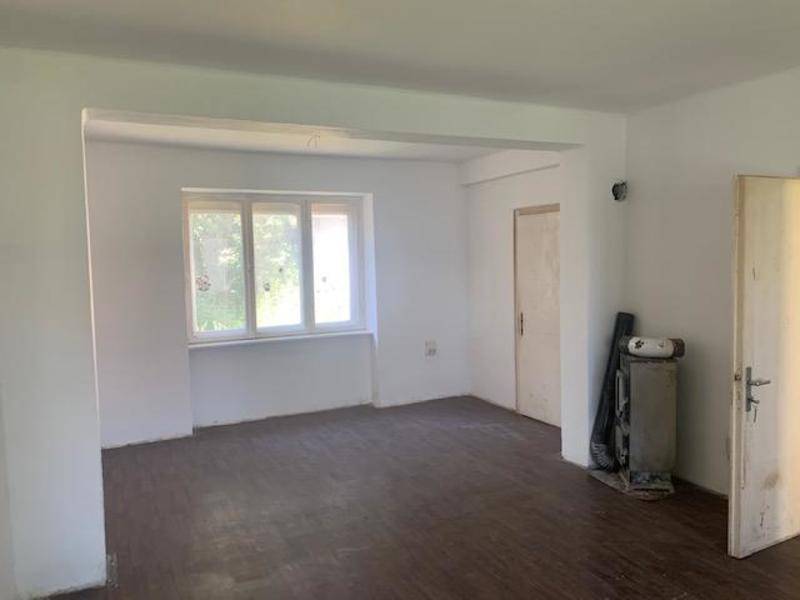 Leerer Raum mit weißen Wänden und dunklem Holzboden, bereit für eine Renovierung.