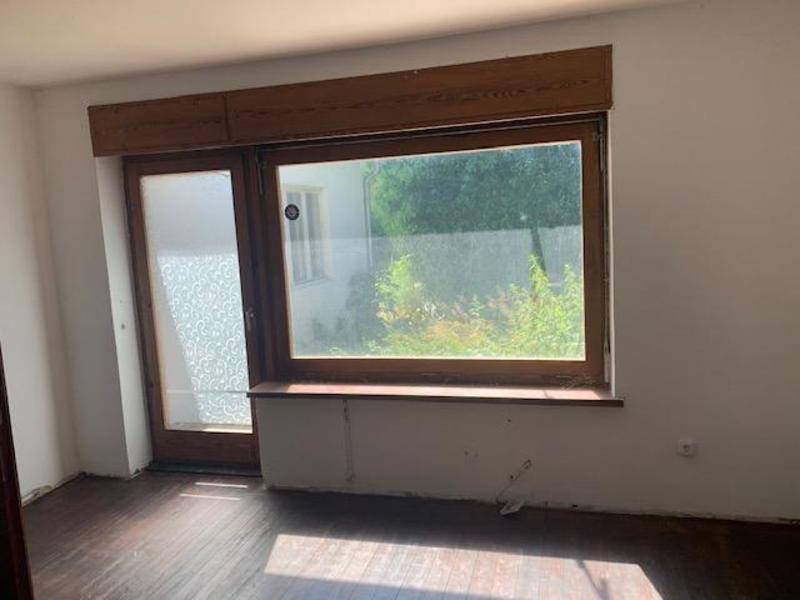 Heller Raum mit großem Fenster und Holzboden, der auf eine Modernisierung wartet.