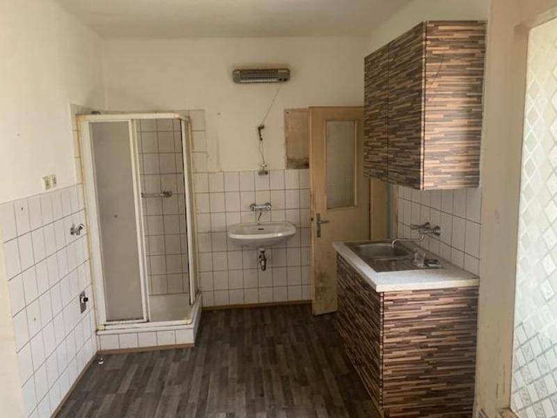 Funktionaler Raum mit Duschkabine, Waschbecken und einfachen Küchenschränken, der eine Modernisierung benötigt.