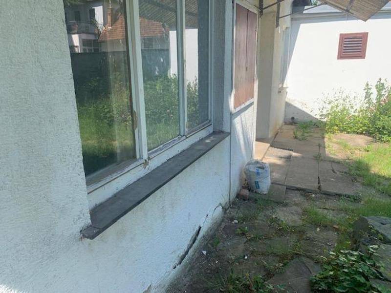 Nahaufnahme einer Hauswand mit Fenster und sichtbaren Schäden am Putz im unteren Bereich.