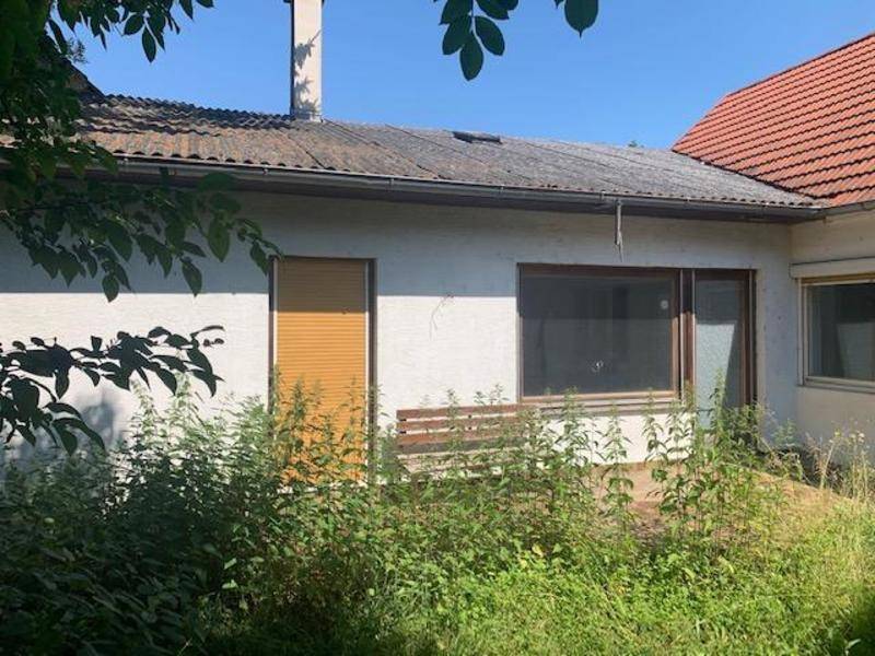 Rückseite eines Hauses mit altem Dach und überwuchertem Gartenbereich, der Pflege benötigt.