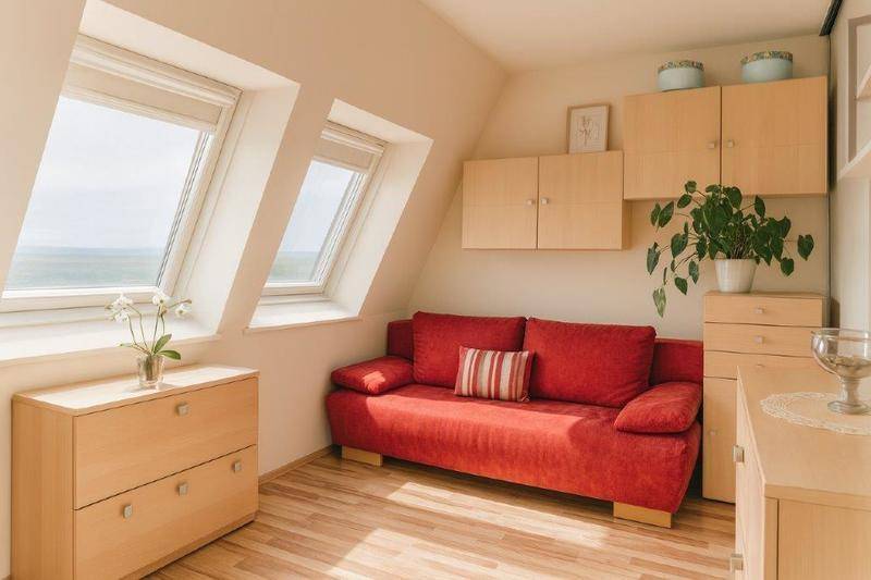 Gemütliches Schlafzimmer mit rotem Sofa, Dachfenstern und hellem Holzmobiliar unter der Dachschräge.