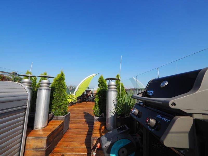 Große Dachterrasse mit Holzboden, Grillbereich und Pflanzen für entspannte Stunden im Freien.