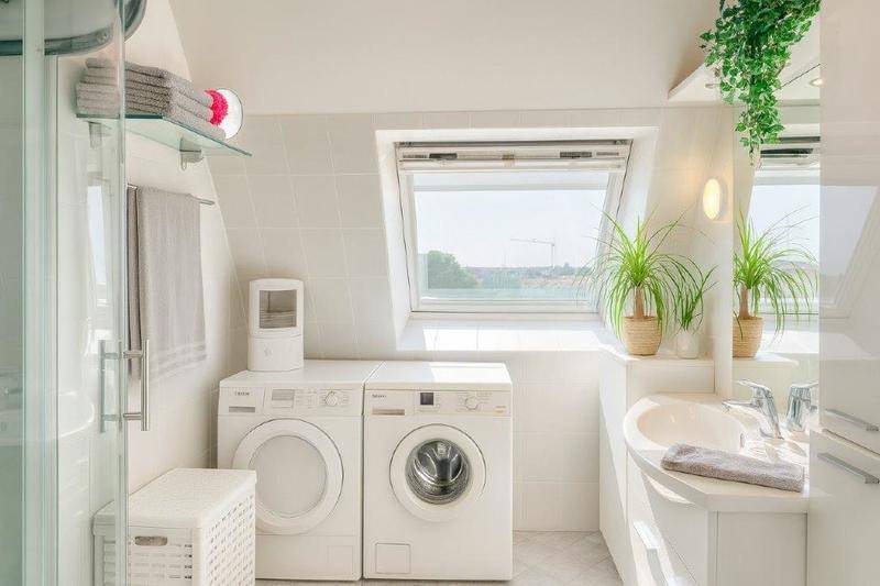 Modernes Badezimmer mit Dachfenster, Waschmaschine, Trockner und Dusche in hellen Farben.