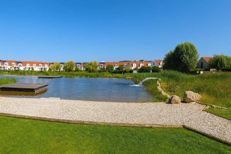 Idyllischer See mit Grünflächen und einer Reihe von Wohnhäusern im Hintergrund.