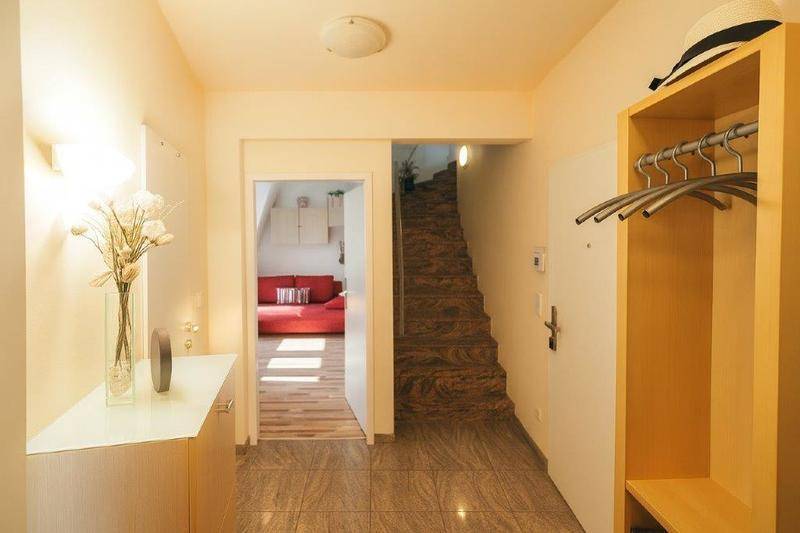 Heller Eingangsbereich mit Fliesenboden, Garderobe und Blick auf eine Holztreppe.