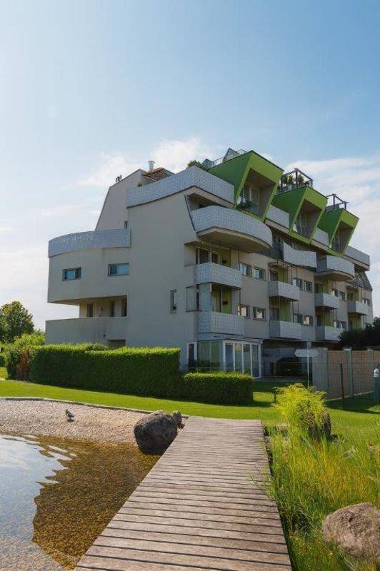 Moderne Wohnanlage mit markanter Architektur, umgeben von Grünflächen und einem Teich.