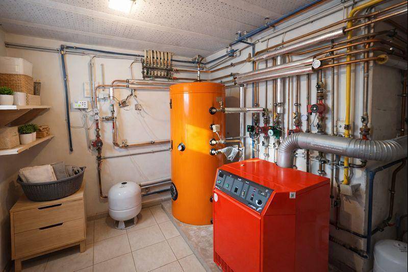 Heizraum im Keller mit Warmwasserspeicher, Heizkessel und sichtbaren Rohren.