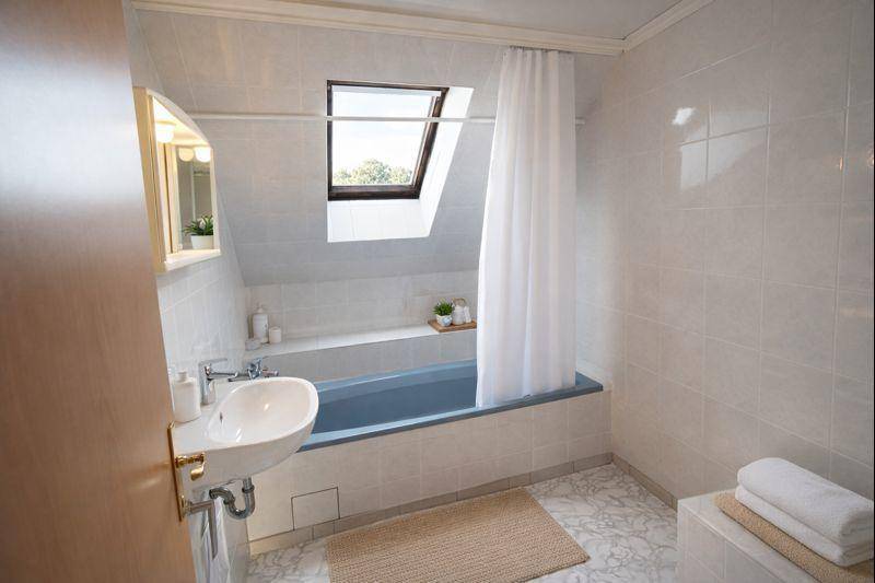 Badezimmer im Dachgeschoss mit Badewanne, Waschbecken, Dachfenster und hellen Fliesen.