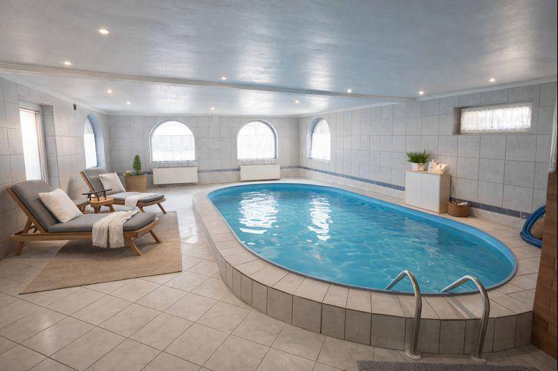 Innenpoolbereich mit Fliesenboden, Liegestühlen und gewölbten Fenstern.