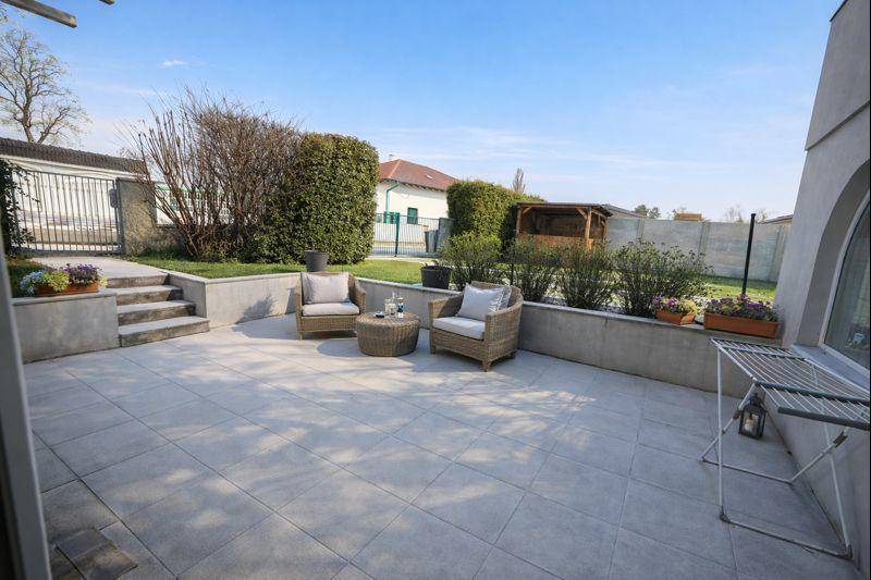 Gepflasterte Terrasse mit Sitzgelegenheiten, Treppe zum Garten und Hecken.