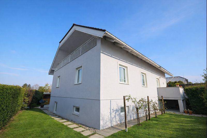 Seitenansicht des Hauses mit gepflegtem Rasen, Balkon und einem kleinen Gartenbereich.