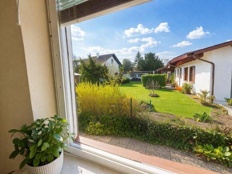 Blick aus dem Fenster auf einen gepflegten Garten mit Rasenfläche und Sträuchern unter blauem Himmel.