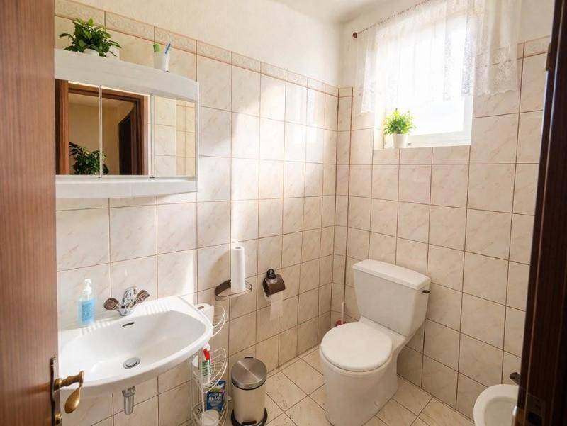Helles WC mit Fliesen an den Wänden, Fenster und einfacher Ausstattung, sauber und funktional.