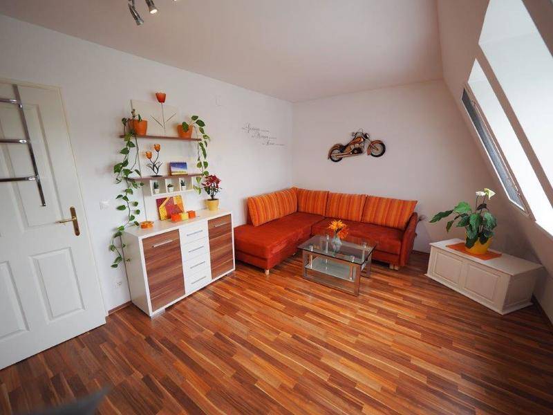 Helles Wohnzimmer mit orangefarbenem Ecksofa, modernem Sideboard und Dachschrägenfenstern auf Holzfußboden.