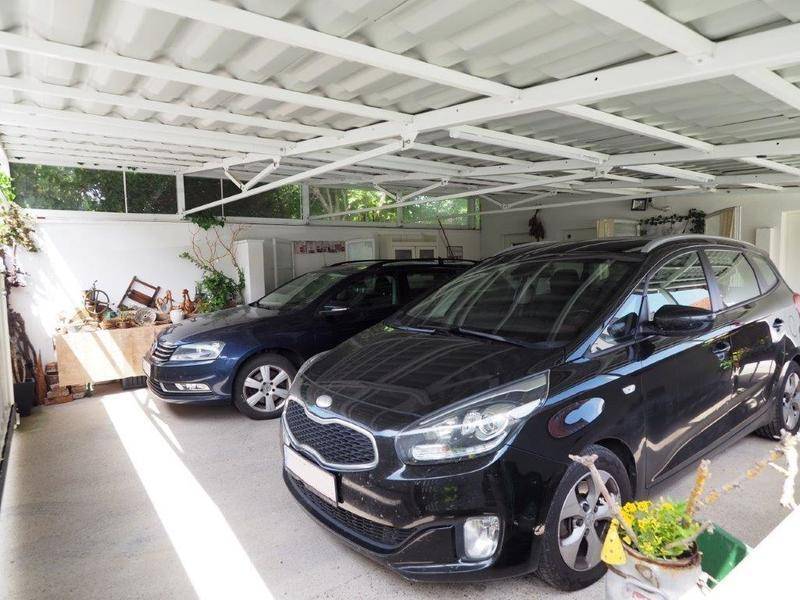 Überdachter Carport mit Platz für zwei Fahrzeuge und zusätzlichem Stauraum im Hintergrund.