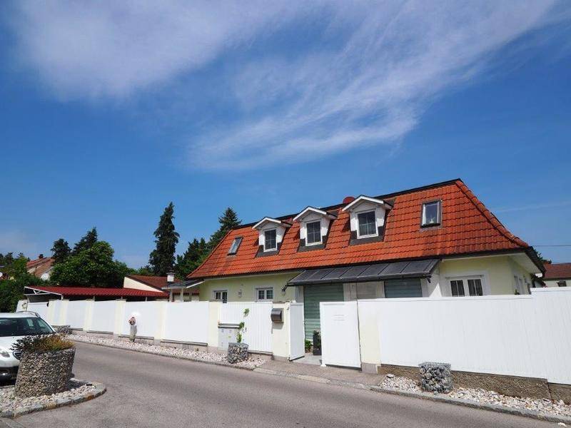 Ansicht des Hauses von der Straße mit rotem Ziegeldach, Gaubenfenstern und weißem Gartenzaun.