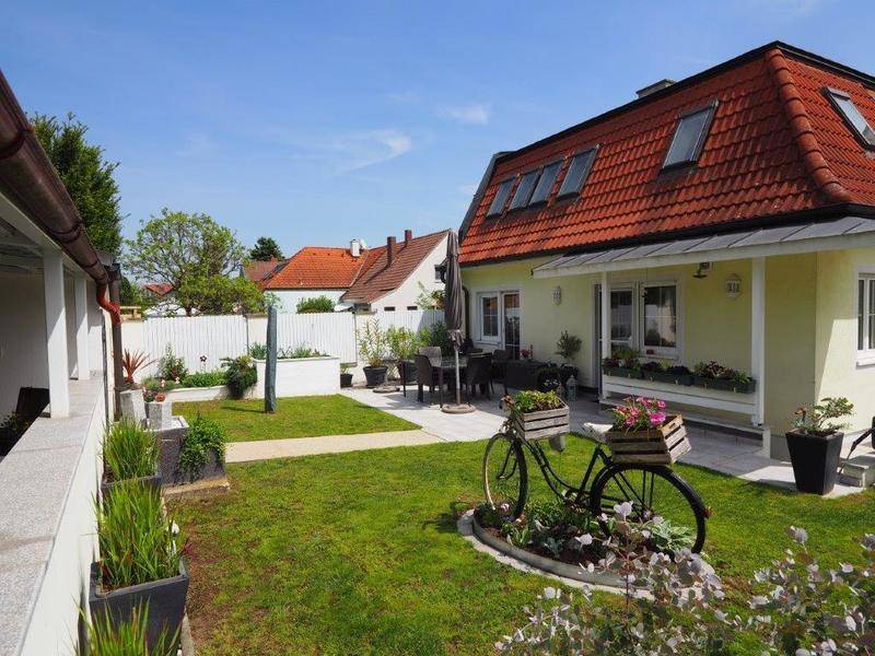 Gepflegter Garten mit Rasenfläche, Terrasse und Sitzbereich neben dem Haus mit rotem Dach.