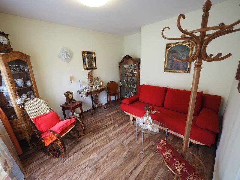 Gemütliches Wohnzimmer mit rotem Sofa, Schaukelstuhl und traditionellen Holzmöbeln auf Laminatboden.